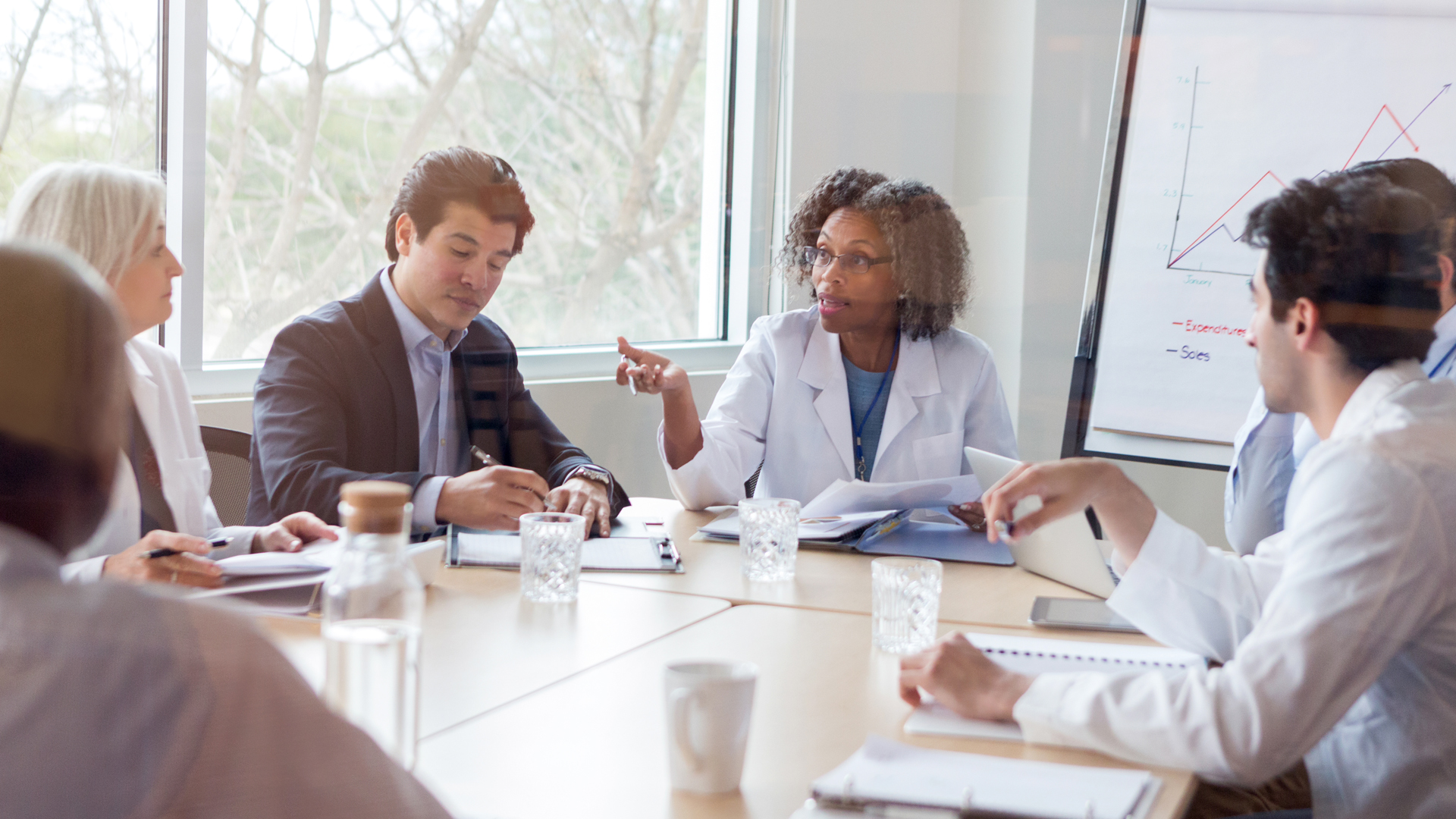 Mature female doctor gestures while discussing something during a healthcare conference with colleagues.